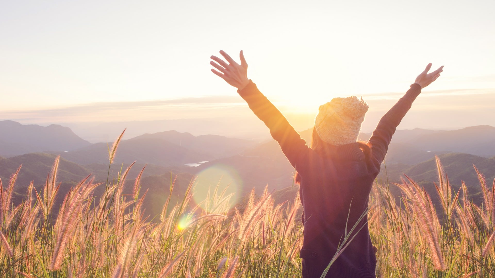 Carefree Happy Woman Enjoying Nature on grass meadow on top of mountain cliff with sunrise. Beauty Girl Outdoor. Freedom concept. Len flare effect. Sunbeams. Enjoyment.